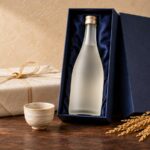 紺色の化粧箱に入った日本酒と酒器、稲穂を並べた贈答イメージ