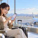 空港でスマートフォンから国内線航空券を予約する旅行者