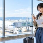 空港でスマートフォンから航空券のキャンセル条件を確認する旅行者