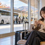 高速バスターミナルの待合室でスマートフォンの予約を確認する旅行者