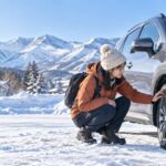 雪山近くのレンタカーでスタッドレスタイヤを確認する旅行者（AI生成イメージ）