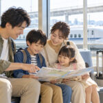新幹線旅行の出発前に駅の待合室で旅程を確認する家族のイメージ（AI生成・架空の風景）