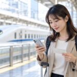 新幹線の駅でスマートフォンと紙のきっぷを確認する旅行者